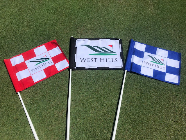 Three flags laying on the green. A red, black, and blue flag.